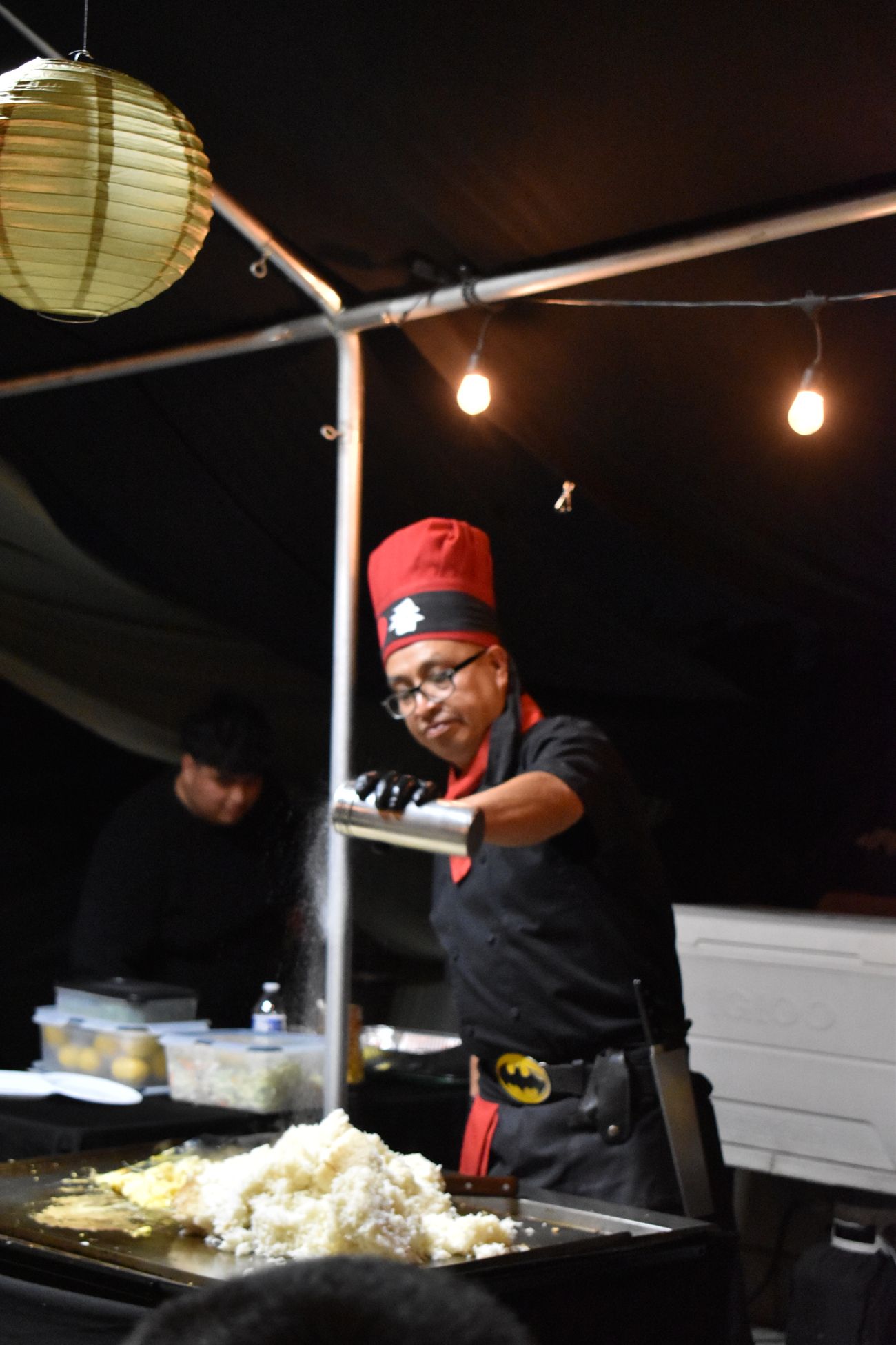 Chef Jorge seasoning fried rice on the grill under string lights